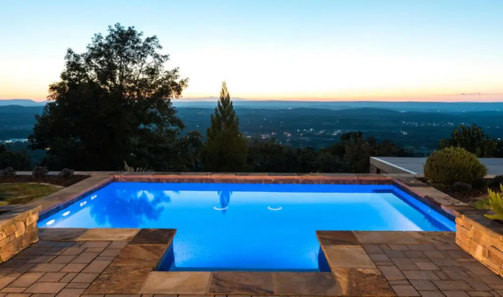 Gunite pool lit blue at dusk with stone coping and a valley view at sunset