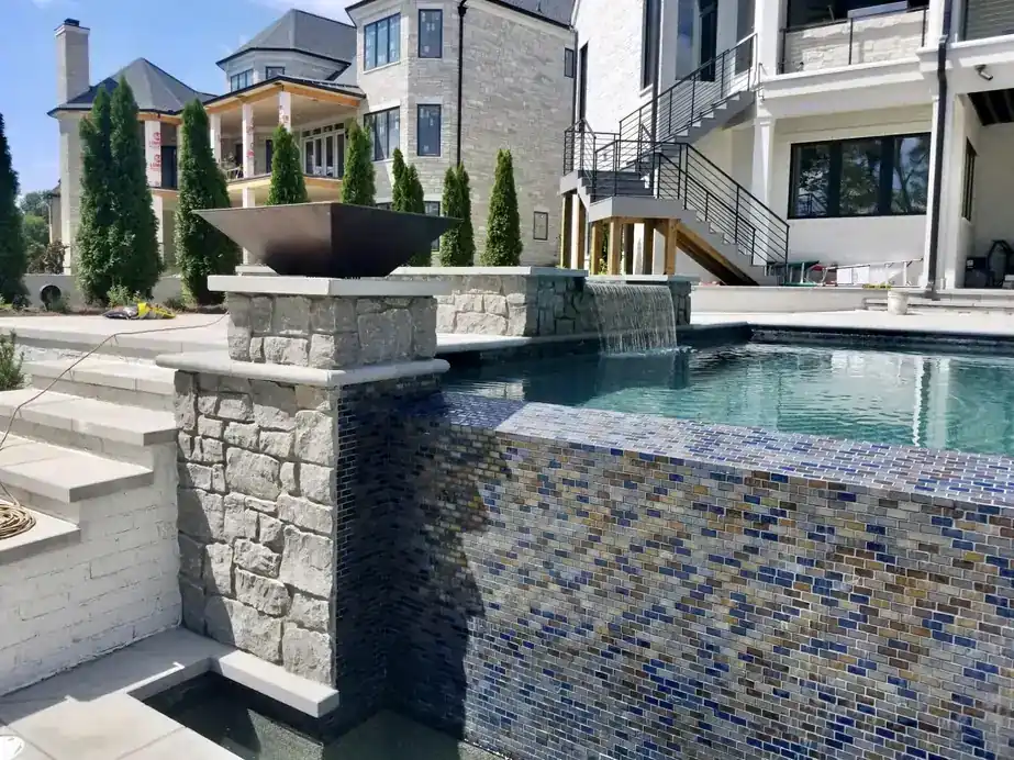 Stacked-stone column with a glass-tile spillway falling into the pool