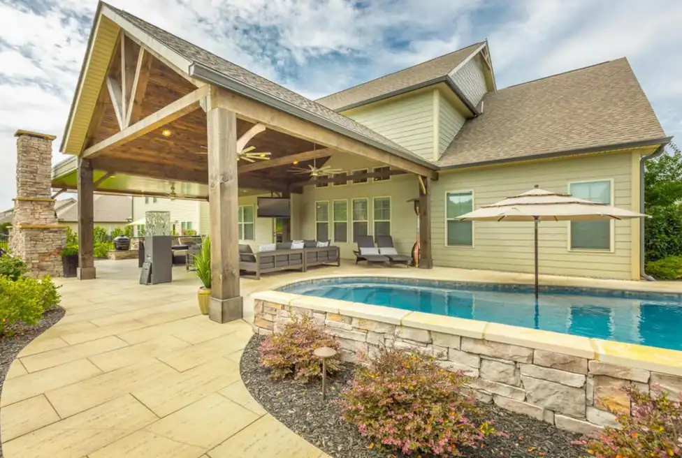 Timber-framed covered porch with a stacked-stone fireplace beside the pool