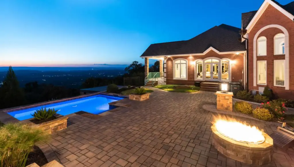 Pool lit blue at dusk beside a brick paver terrace and a gas fire pit with a valley view