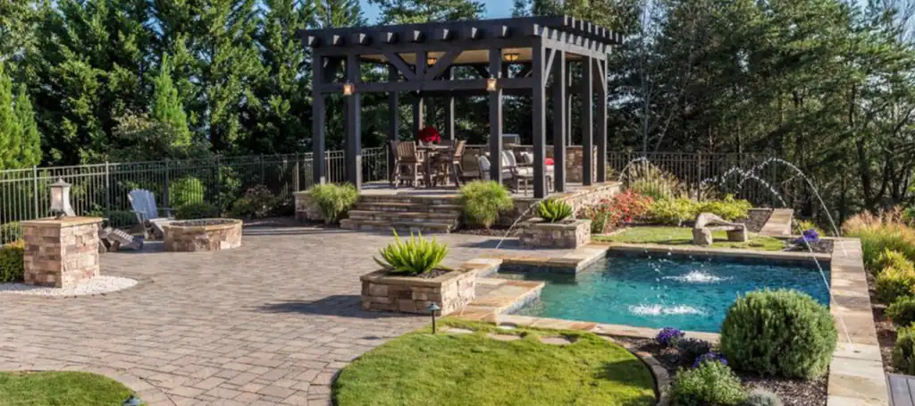 Paver patio with a pergola, a stone fire pit and laminar jets arcing into the pool