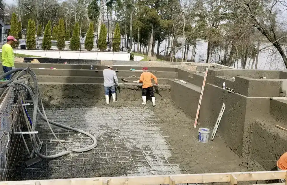 Crew shooting gunite over a rebar cage on a hillside pool site