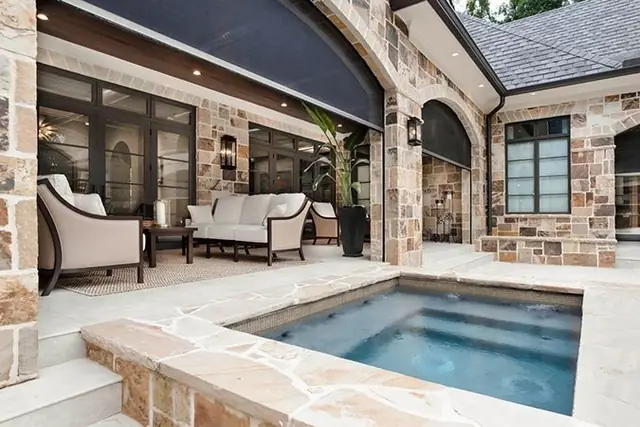 Stone-clad covered porch with lounge seating beside a sunken spa