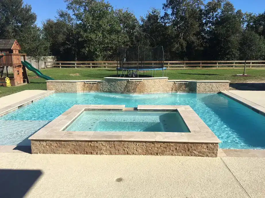 Pool with a raised spa and a stacked-stone wall, a backyard play set in the trees behind