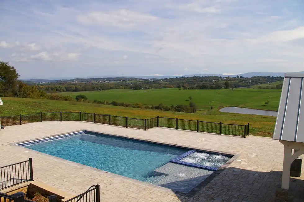 Rectangular pool with a spa spillway and a paver deck looking out over open Tennessee pasture
