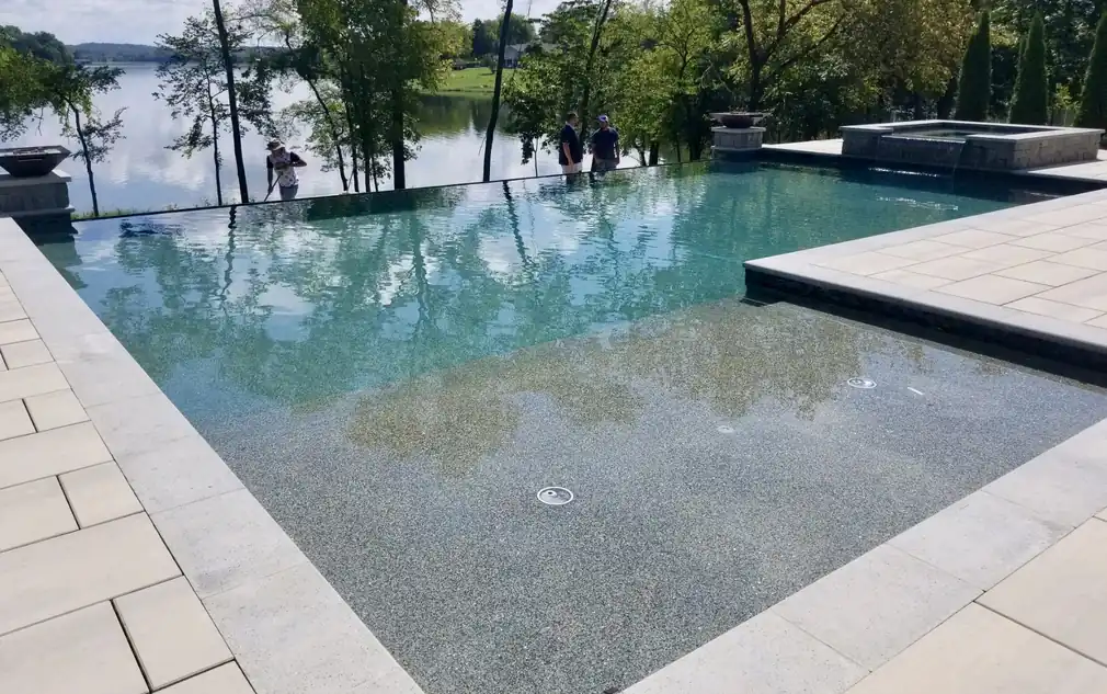 Infinity-edge pool and raised spa set in large-format pavers above a lake